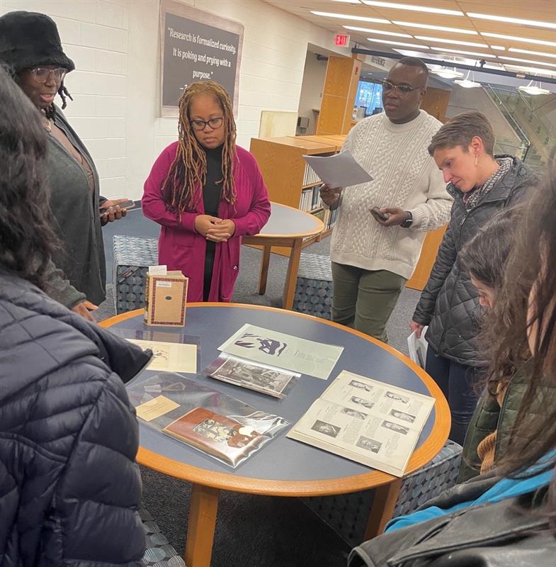 A group of people stand around a table looking at a collection of books