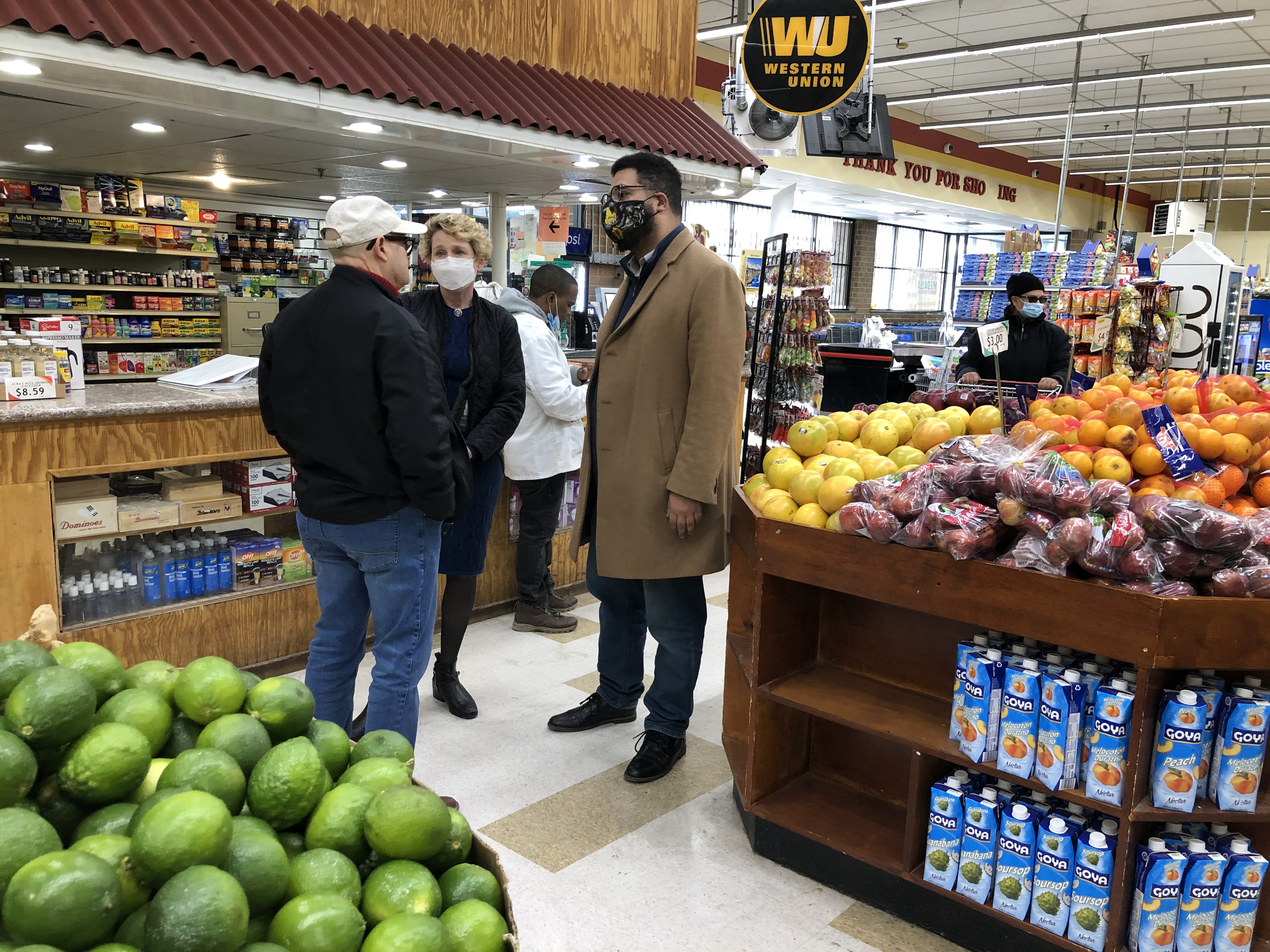 Three people speak, surrounded by produce