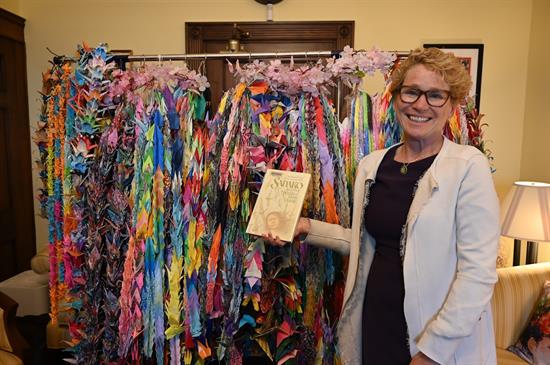 Rep. Houlahan holds up the book Sadakao and the Thousand Cranes in front of a coat rack covered in paper cranes of all colors