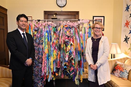 Rep. Houlahan stands with a man in a business suit in front of a coat rack covered in colorful paper cranes